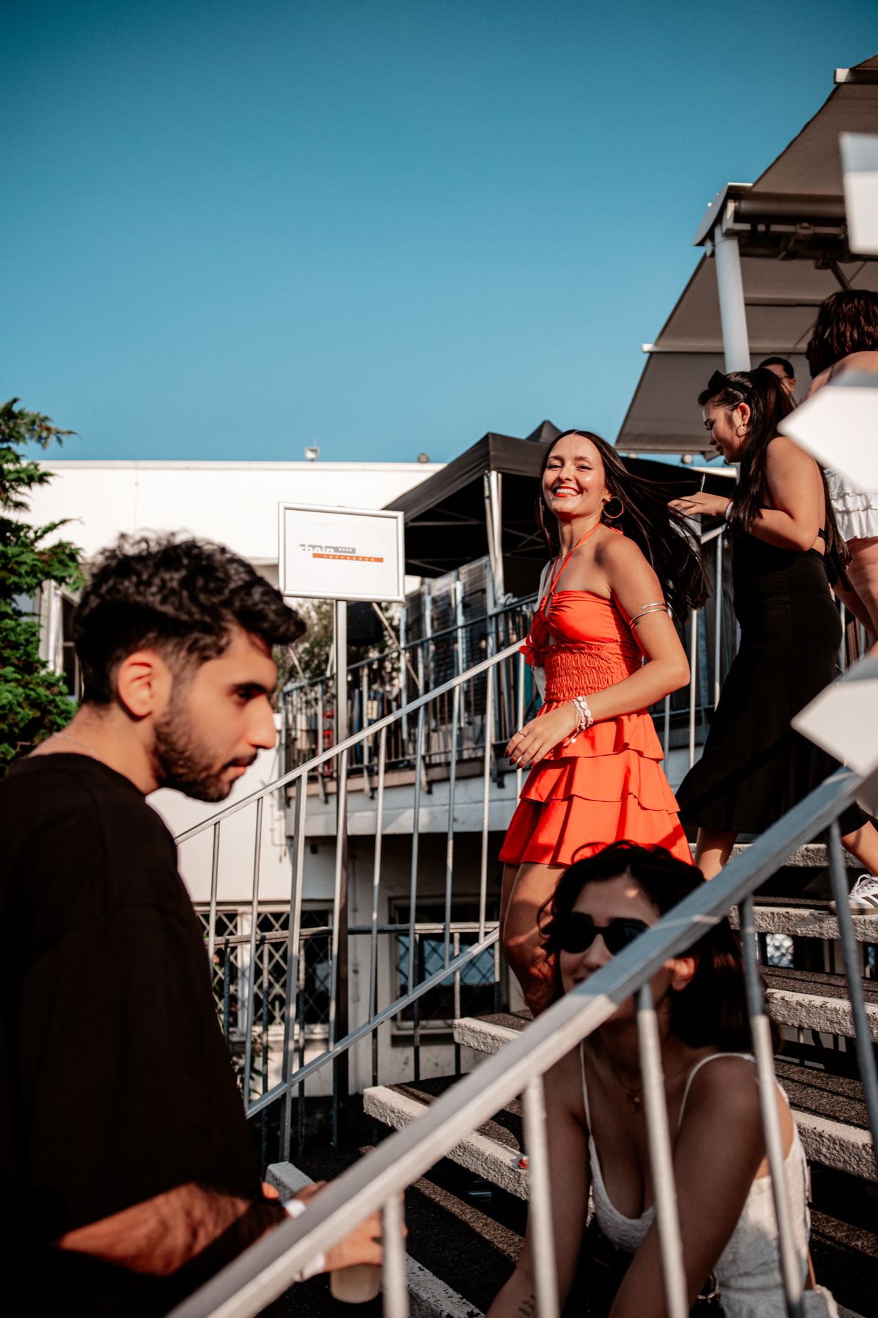 Frau im orangen Sommerkleid lacht auf der Treppe der Rheinterrassen Köln unter blauem Himmel