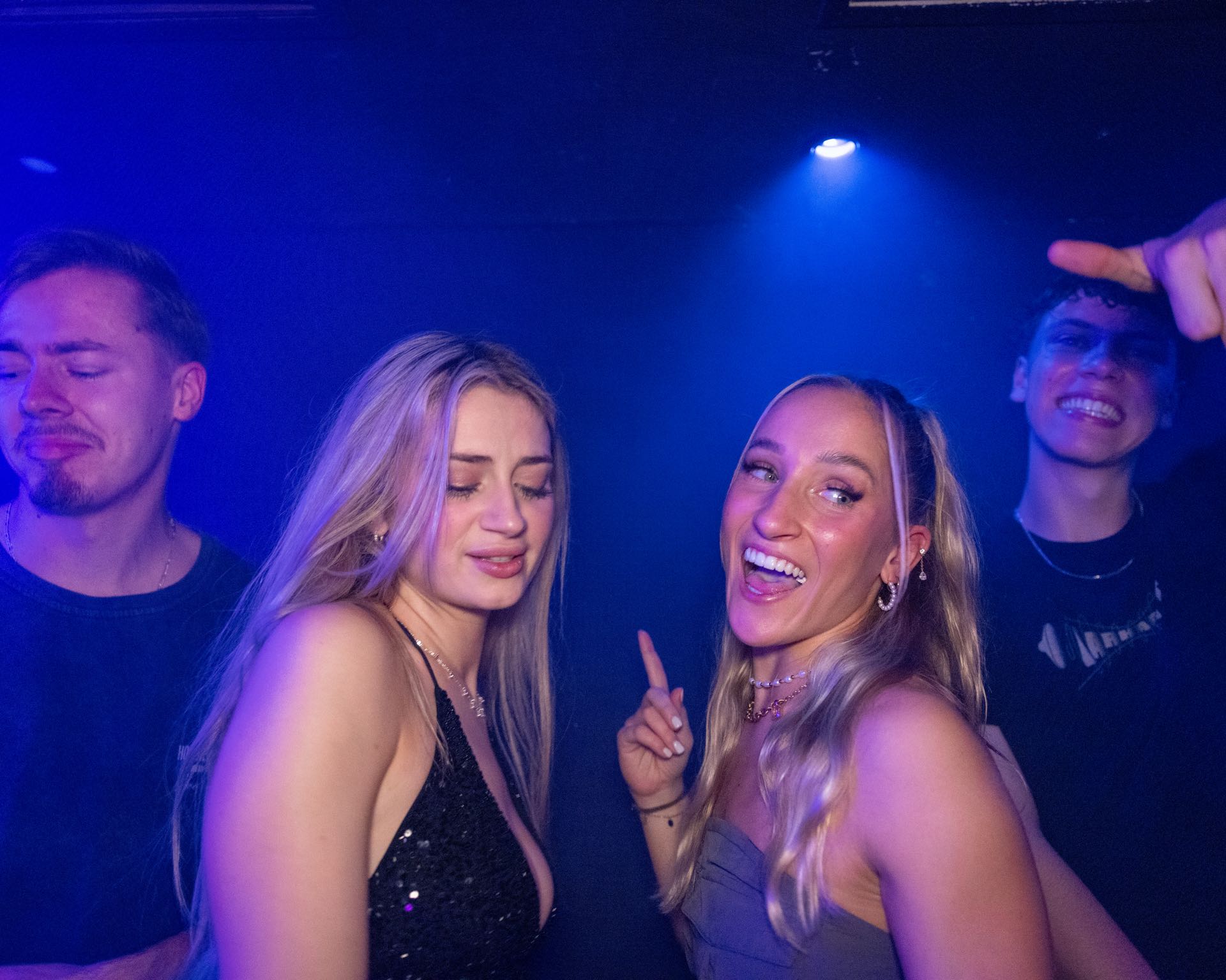 Vier Freunde tanzen und lachen zusammen im blauen Licht auf der Tanzfläche einer Golden Flame Club-Nacht in Köln