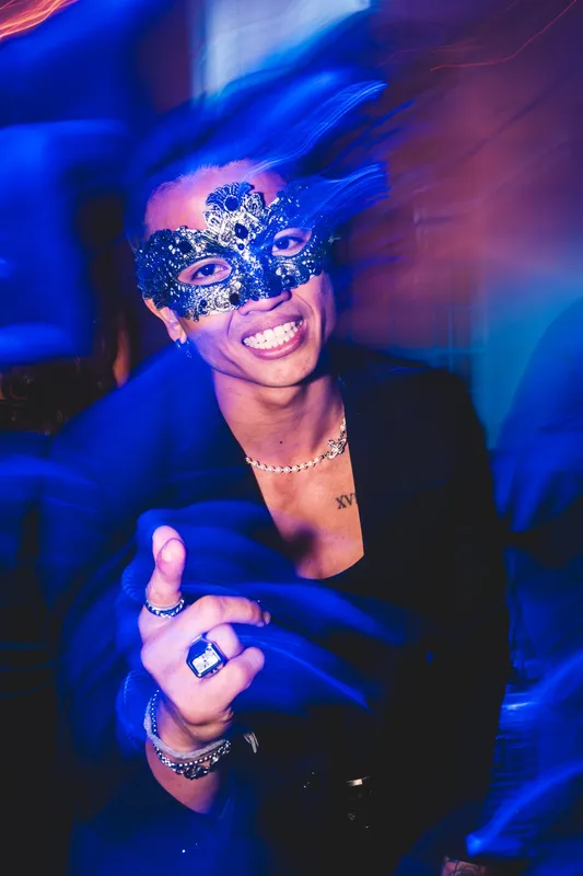 Lachender Gast mit schwarzer Spitzenmaske in blauem Licht beim Maskenball Golden Mask in der Flora Köln