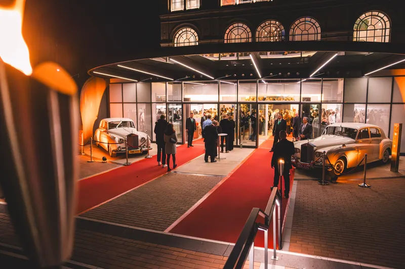 Roter Teppich und zwei Oldtimer vor dem beleuchteten Eingang der Flora Köln am Abend des Maskenballs Golden Mask