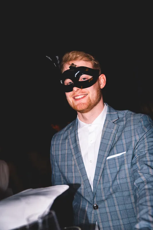 Lachender Gast im karierten Anzug mit schwarzer Maske beim Maskenball Golden Mask in der Flora Köln