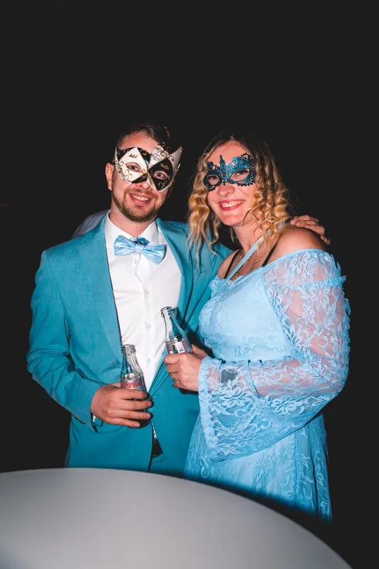 Paar mit Masken beim Golden Mask: er im türkisen Anzug mit hellblauer Fliege, sie im hellblauen Spitzenkleid mit blauer Maske