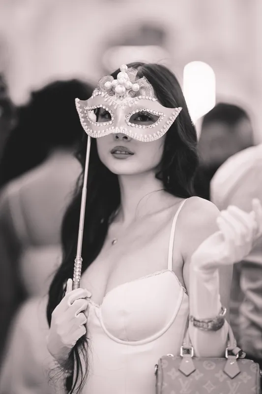 Schwarz-Weiß-Foto einer Frau mit weißer Maske am Stab, Korsagen-Top und langen weißen Handschuhen beim Golden Mask