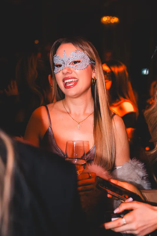 Lachende Frau mit silberner Glitzer-Halbmaske und Glas beim Maskenball Golden Mask in der Flora Köln