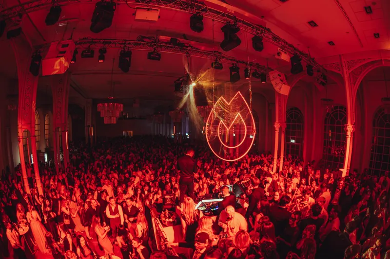Voller Festsaal in rotem Licht mit leuchtendem Flammen-Logo beim Golden Mask in der Flora Köln