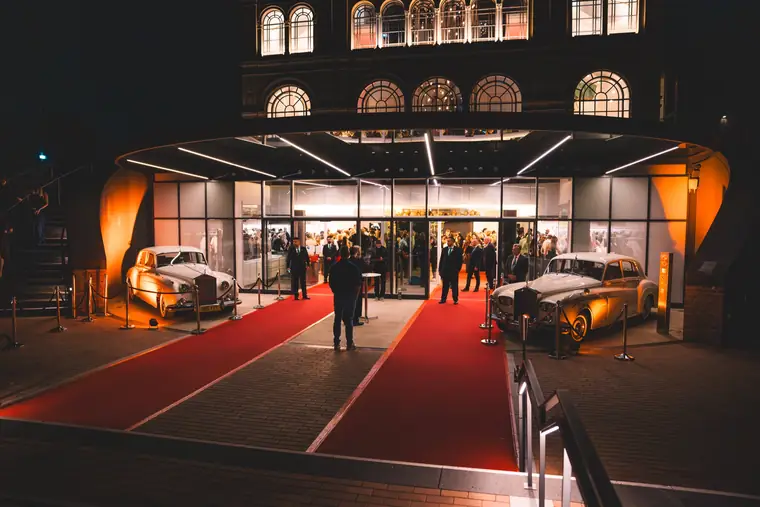 Red carpet and vintage cars in front of the lit entrance of the Flora in Cologne in the evening