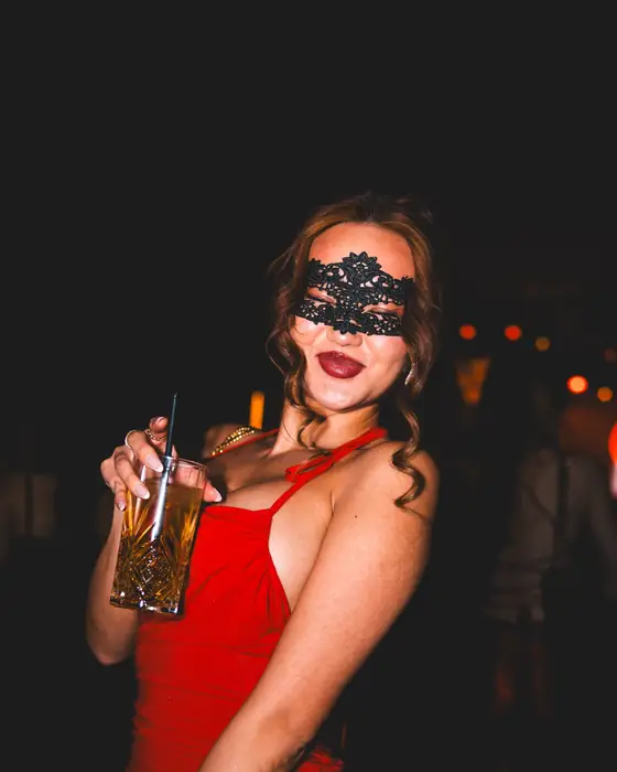 Frau mit langen dunklen Locken, schwarzer Spitzenmaske und rotem Lippenstift im roten Kleid beim Golden Mask