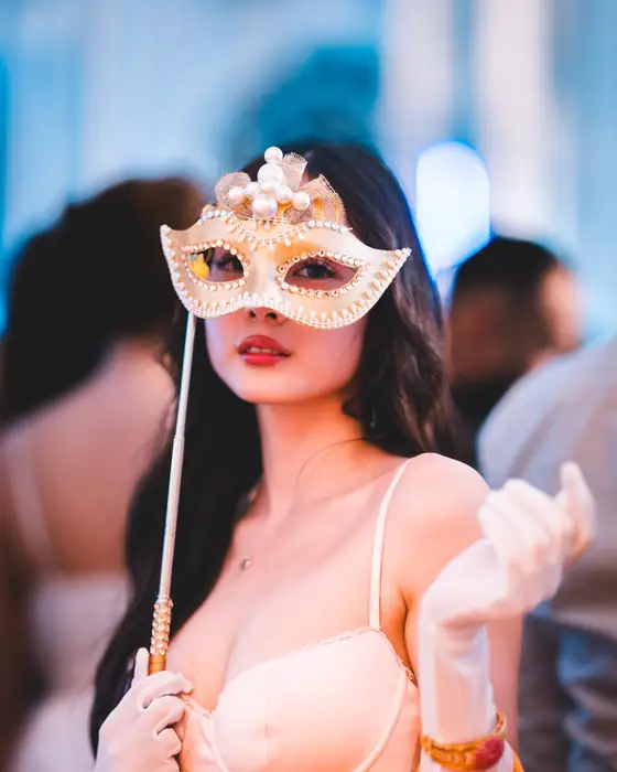 Frau hält eine weiße, mit Perlen verzierte Maske am Stab vor das Gesicht, dazu weiße Handschuhe, beim Golden Mask in Köln