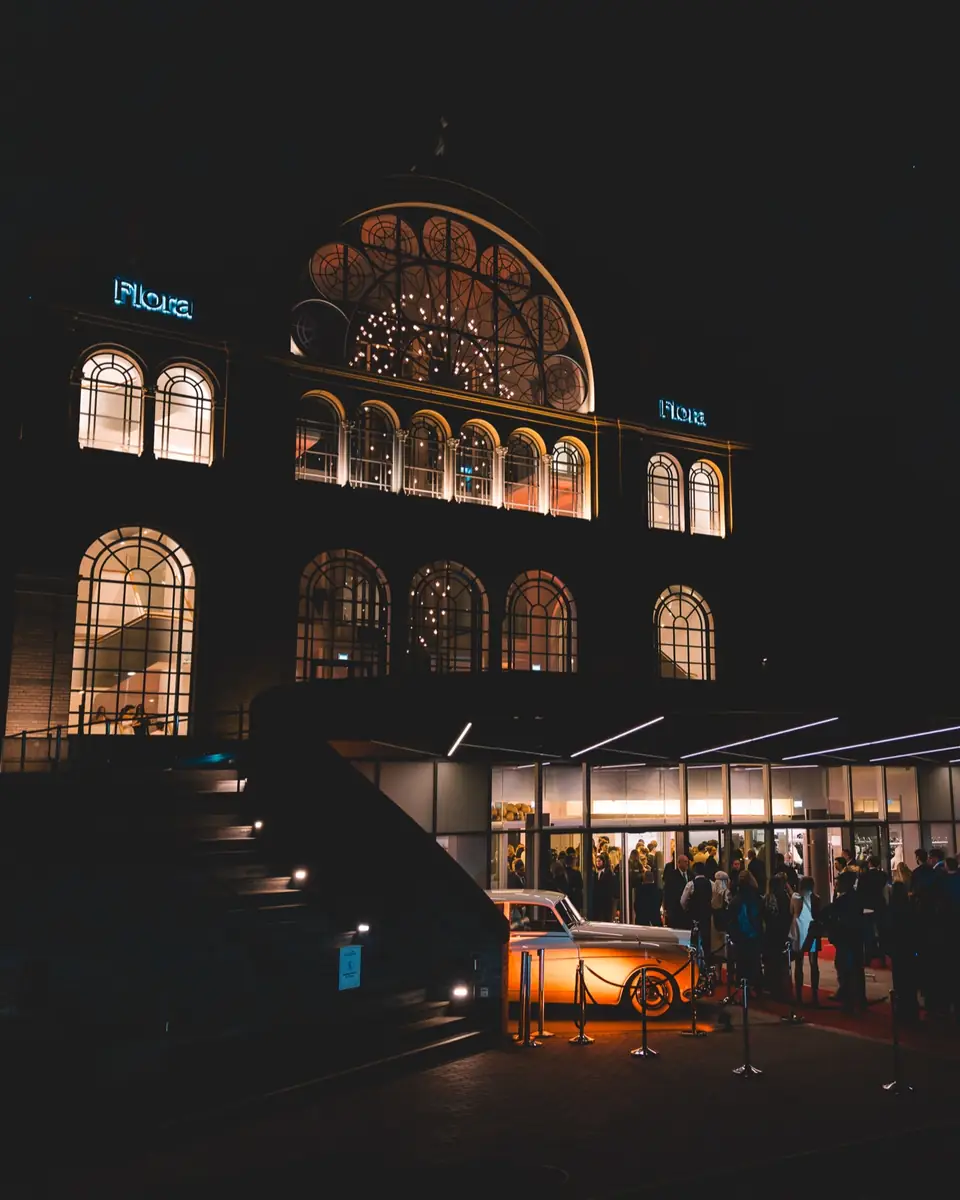 Die Flora Köln bei Nacht, warm beleuchteter Eingang und Gäste in der Ferne