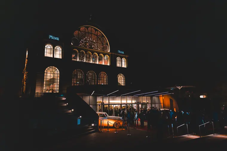 Die Flora Köln bei Nacht, warm beleuchteter Eingang und Gäste in der Ferne