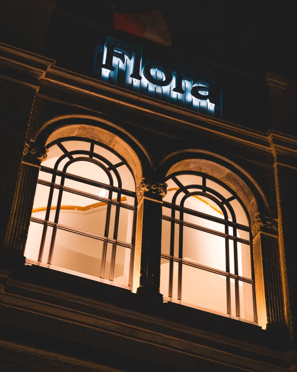 Zwei warm beleuchtete Rundbogenfenster der Flora Köln bei Nacht, darüber der Schriftzug Flora