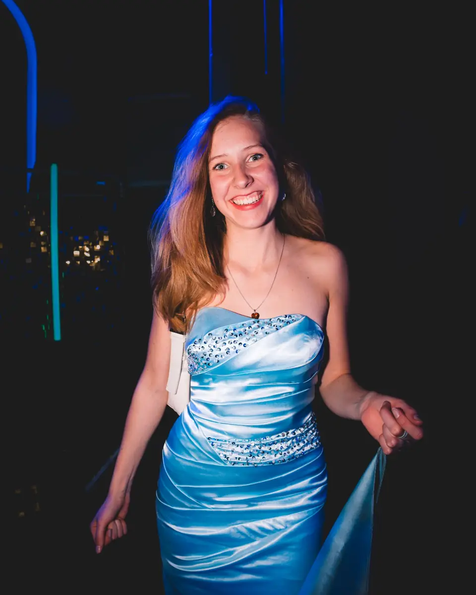 Lachende junge Frau in einem trägerlosen hellblauen Satinkleid mit glitzernden Details beim Maskenball Golden Mask in der Flora Köln