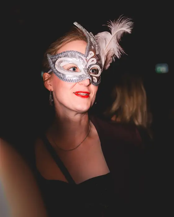 Frau mit silberner Halbmaske mit weißen Federn im Stil einer Colombina beim Maskenball Golden Mask in Köln