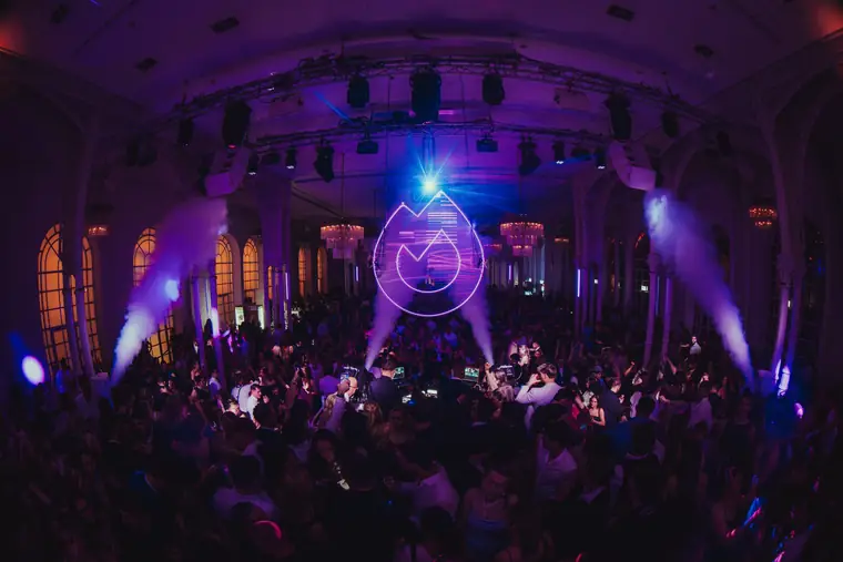 Festsaal in violettem Licht mit leuchtendem Flammen-Logo und voller Tanzfläche bei Golden Mask