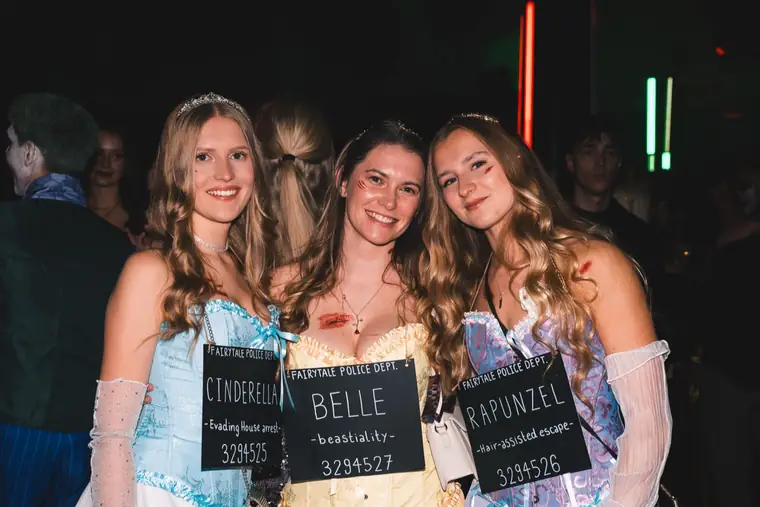 Three friends dressed as Cinderella, Belle and Rapunzel holding mugshot boards at the Halloween party Spooky Flame in Cologne