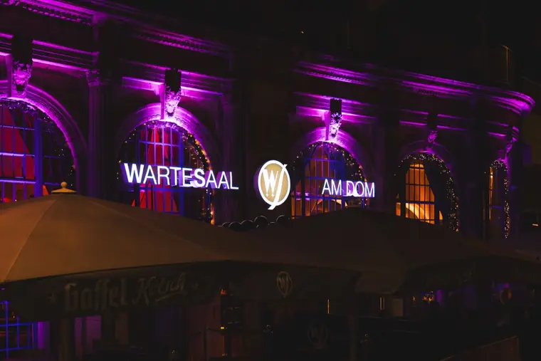 Fassade des Wartesaals am Dom in lila Licht mit Leuchtschrift am Abend der Halloween-Nacht Spooky Flame
