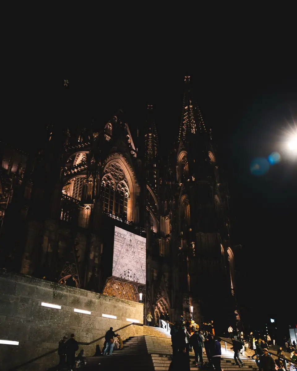 Der beleuchtete Kölner Dom bei Nacht, davor eine breite Steintreppe mit Menschen