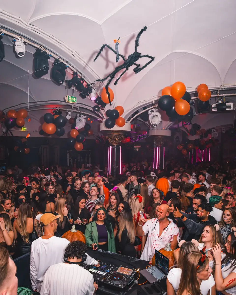 Volle Tanzfläche im Wartesaal am Dom bei Spooky Flame: Riesenspinne unter der Gewölbedecke, orange und schwarze Ballons, Gäste in Kostümen