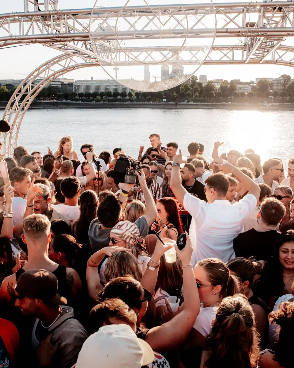 Feiernde Crowd mit erhobenen Händen unter dem Bühnenbogen am Rhein in Köln