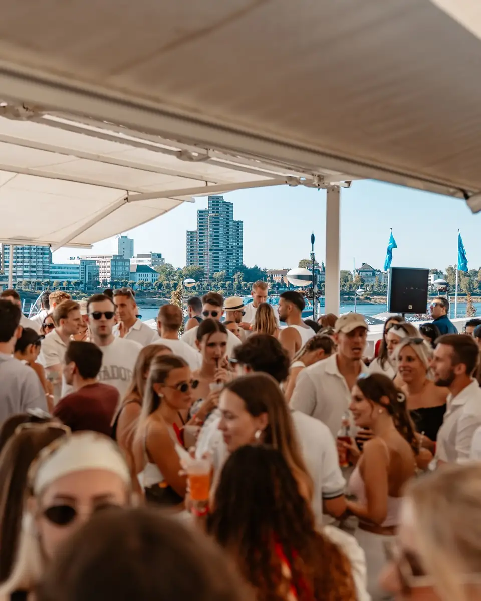 Volle Terrasse unter dem Sonnensegel beim Golden Flame Open-Air an den Rheinterrassen Köln, im Hintergrund Rhein und Skyline
