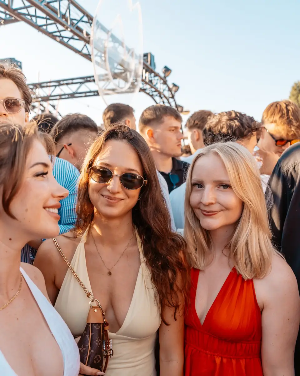 Drei Freundinnen in Sommerkleidern lachen im goldenen Abendlicht beim Golden Flame Open-Air an den Rheinterrassen Köln