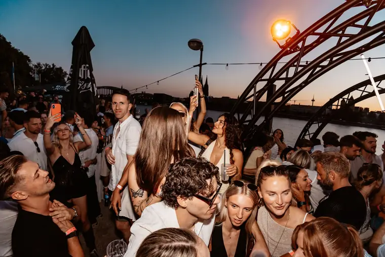 Crowd im Gegenlicht der untergehenden Sonne unter dem Flammen-Bogen am Rhein in Köln