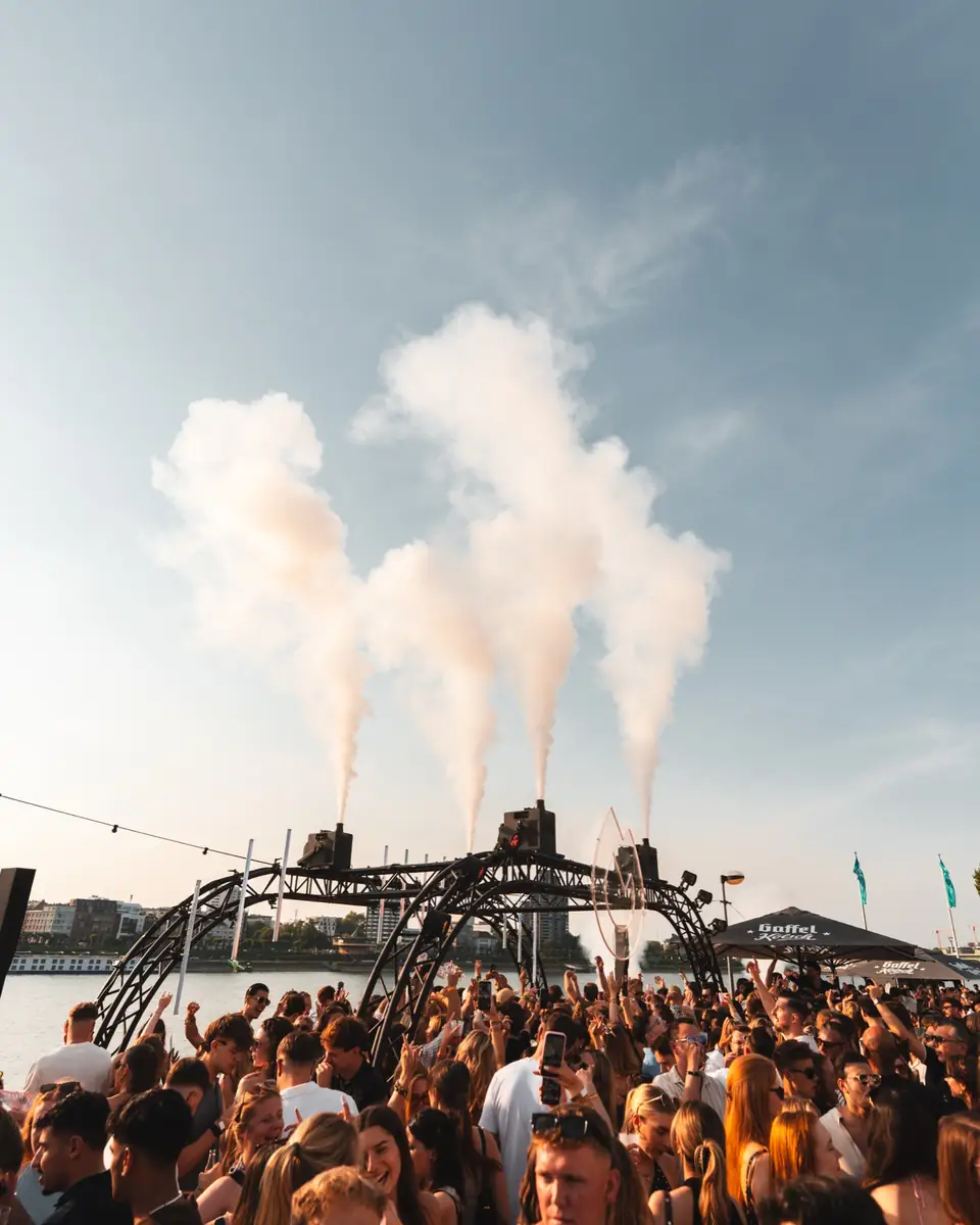 Nebelfontänen steigen in den blauen Himmel über der Crowd beim Golden Flame Summer Opening am Rhein