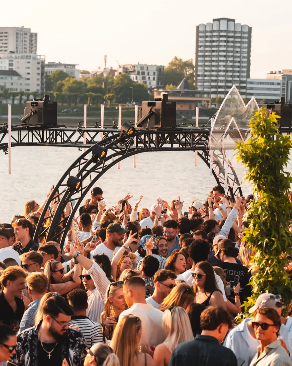 Crowd under the stage arch on the Rhine with the Cologne skyline behind, at the Golden Flame Summer Opening