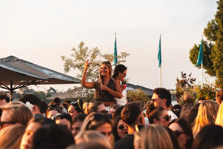 Feiernde Crowd zwischen Sonnenschirmen und Fahnen auf der Terrasse am Rhein beim Golden Flame Summer Opening