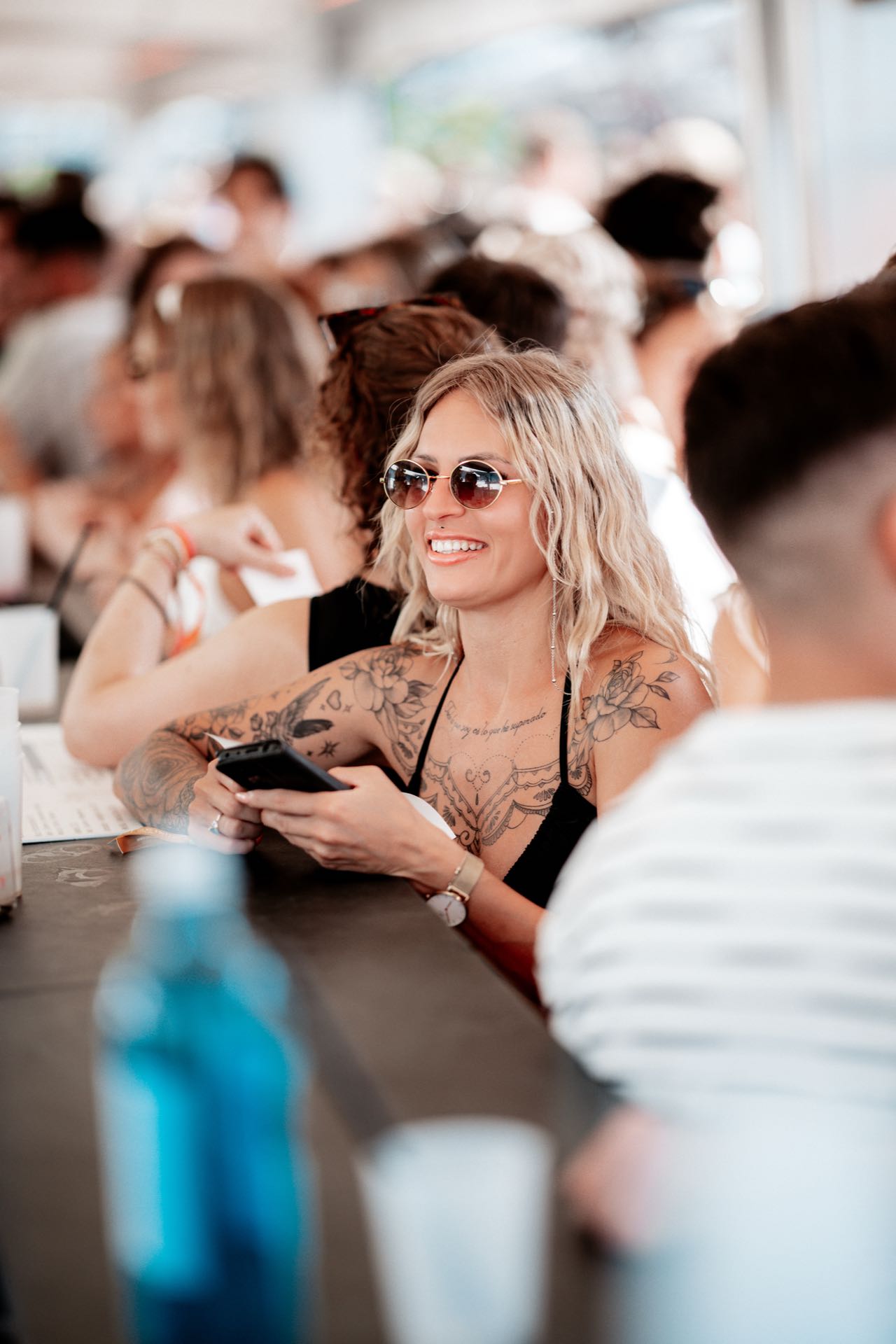 Junge Frau mit Sonnenbrille sitzt lachend mit ihren Freundinnen am langen Tisch beim Golden Flame Open-Air in Köln