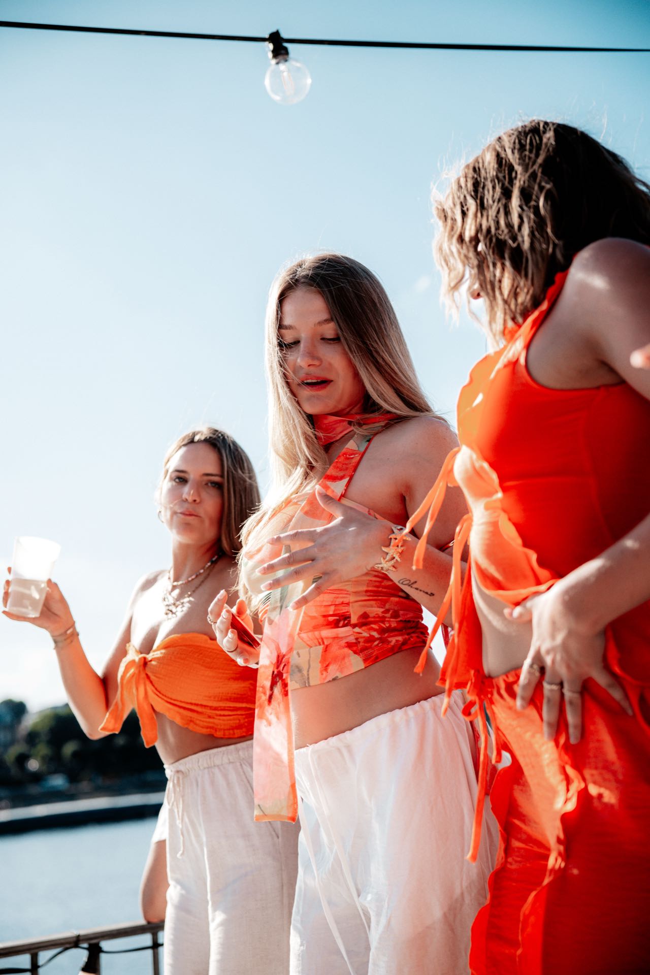 Drei Freundinnen in abgestimmten Orange-Looks stehen zusammen am Rheinufer beim Golden Flame Open-Air in Köln
