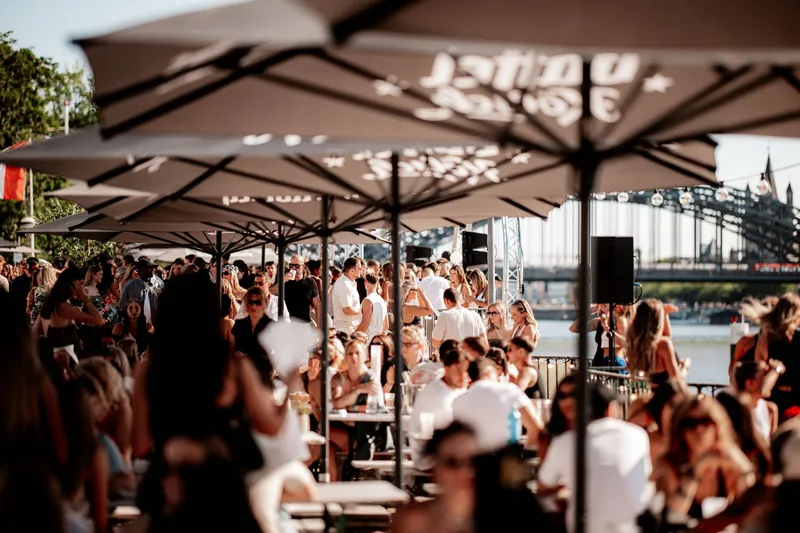 Sonnenschirme und Gäste auf der Terrasse der Rheinterrassen mit Blick auf die Hohenzollernbrücke