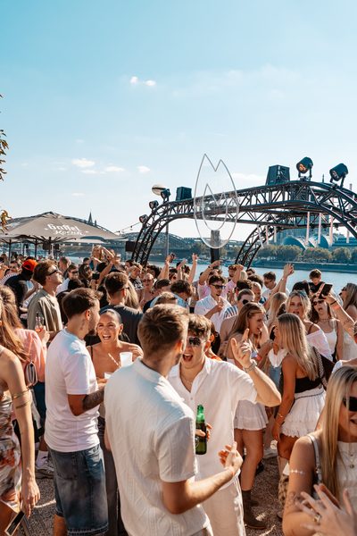 Volle Tanzfläche am Nachmittag beim Golden Flame Open-Air am Rhein in Köln mit Flammen-Bogen