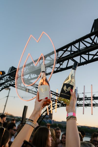 Zwei Flaschen Engel und Flamme Rosé und Weißwein vor dem leuchtenden Flammen-Logo beim Golden Flame Open-Air Köln