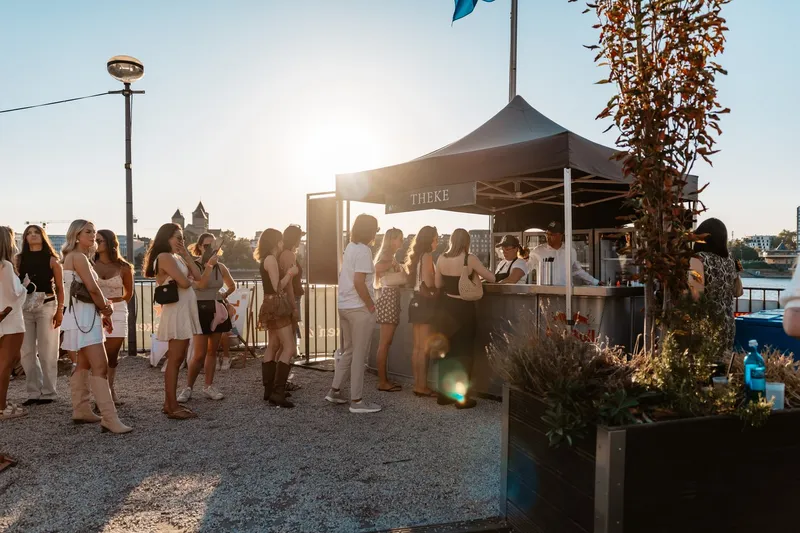 Gegenlicht der Sonne hinter einem Pavillon, Gäste als Silhouetten auf dem Sand am Rhein
